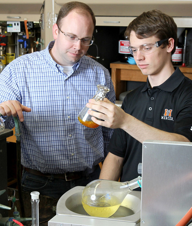 Faculty member and student looking at beaker of liquid